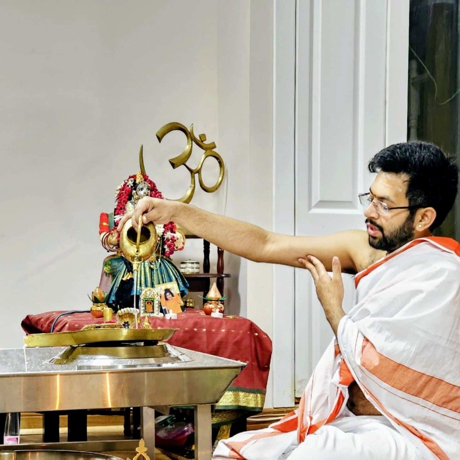 Purohit Surya performing abhishekam over a Shiva Lingam at a home altar